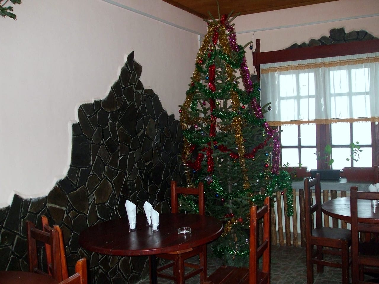 Peretele-relief de piatră închisă la culoare din sala restaurantului, cu bradul împodobit alături.